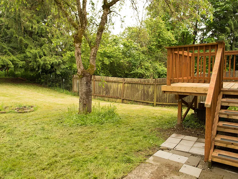 Large private backyard with mature trees, fenced outdoor space, and raised deck area perfect for relaxing, entertaining, or outdoor dining.