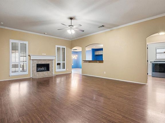Unfurnished living room with ceiling fan, healthy amount of natural light, wood finished floors, a fireplace, and crown molding