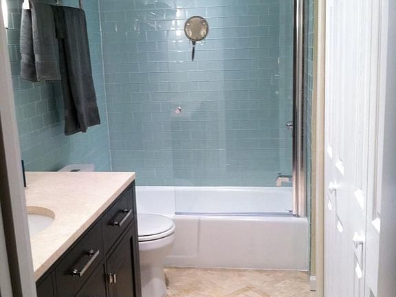 Renovated bathroom with glass subway tile and marble floor and vanity.