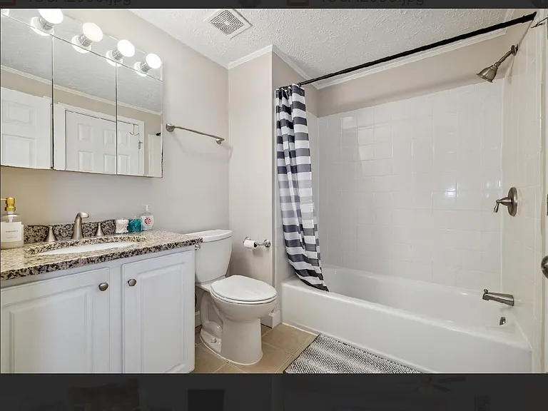 Full bathroom with a tub/shower combo, granite-look vanity countertop, mirrored medicine cabinet, and tile flooring.