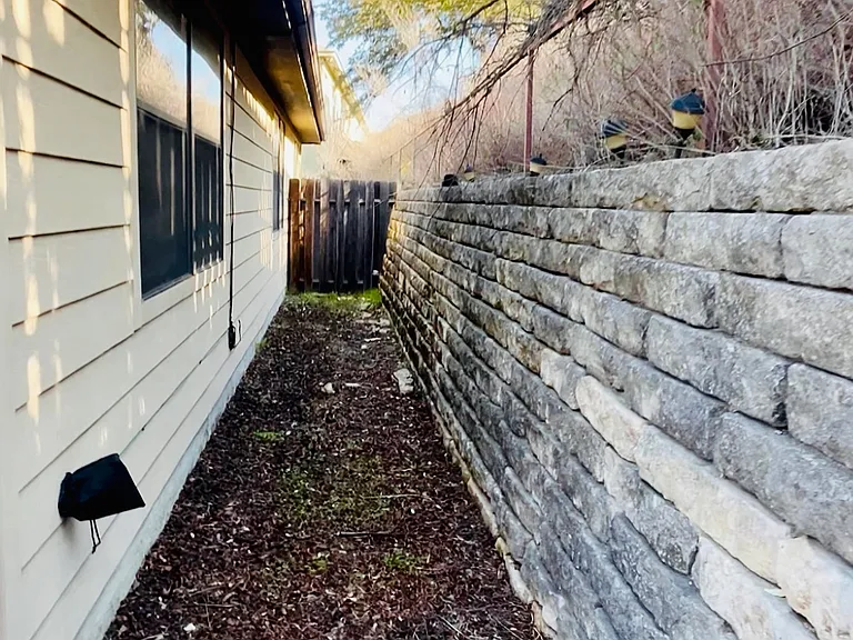 Private fenced backyard featuring a stone retaining wall and side walkway