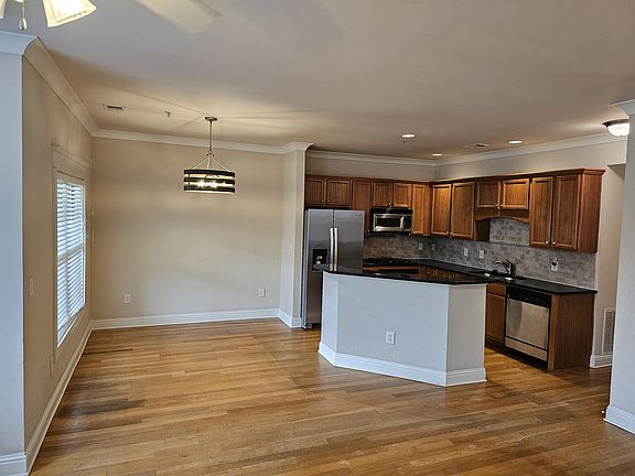 Stylish open-concept kitchen and living space featuring hardwood floors, stainless steel appliances, black countertops, and a tiled backsplash designed for both functionality and flow.