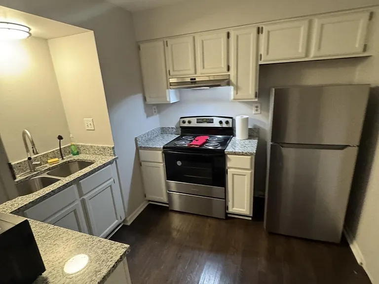 Efficient galley kitchen with ample cabinetry, granite-look counters, double sink, and stainless fridge with electric range.