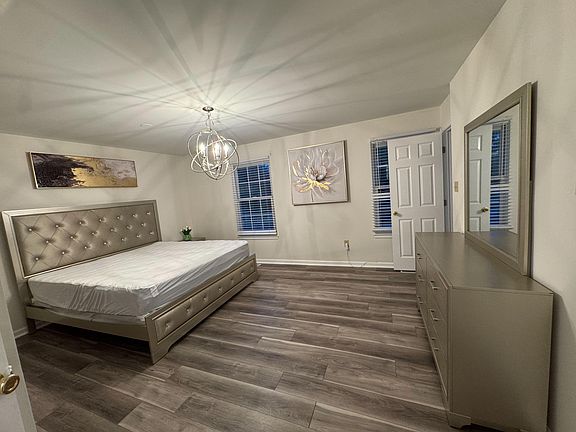 Spacious bedroom with plank flooring, dual windows, a stylish overhead light, and a dresser with mirror for storage.