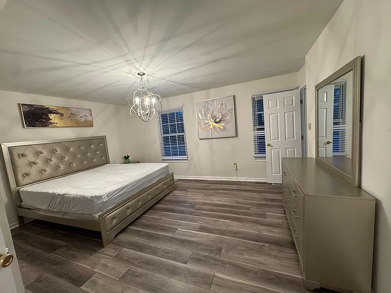 Spacious bedroom with plank flooring, dual windows, a stylish overhead light, and a dresser with mirror for storage.