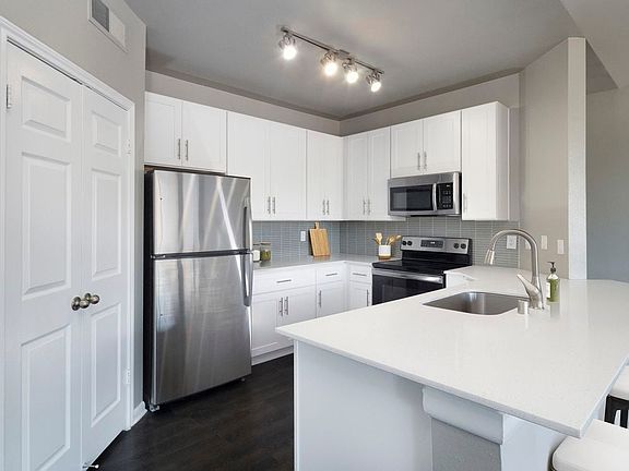 Classic Package II kitchen with stainless steel appliance, white quartz countertop, tile backsplash, white cabinetry, and hard-surface flooring