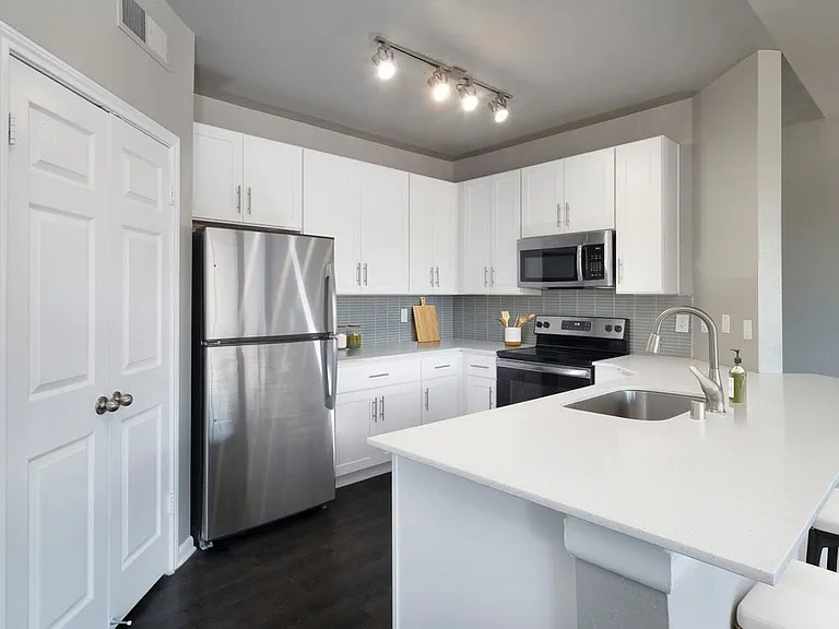Classic Package II kitchen with stainless steel appliance, white quartz countertop, tile backsplash, white cabinetry, and hard-surface flooring