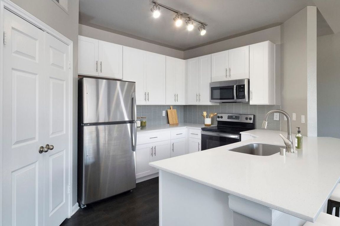 Classic Package II kitchen with stainless steel appliance, white quartz countertop, tile backsplash, white cabinetry, and hard-surface flooring