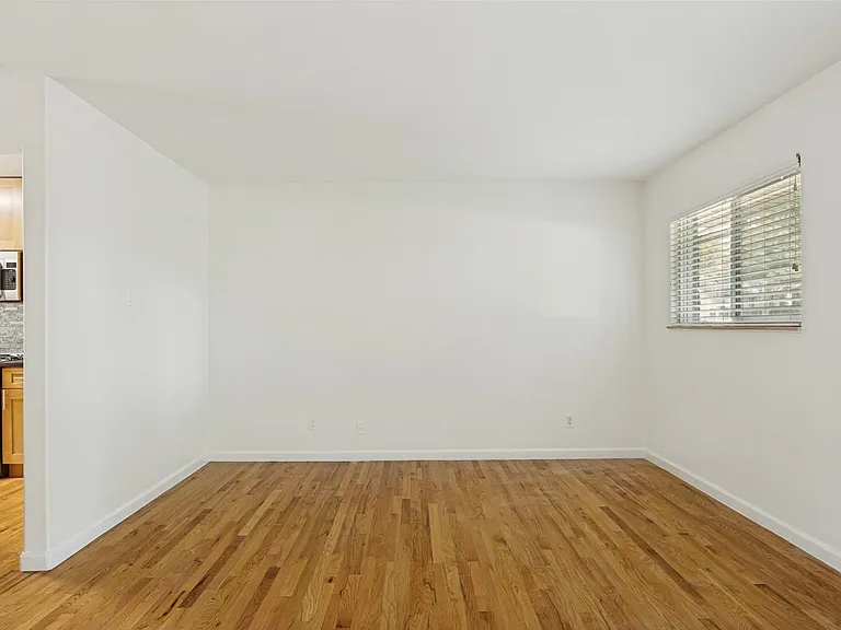 Spacious room featuring wood-finish flooring and a large window with horizontal blinds