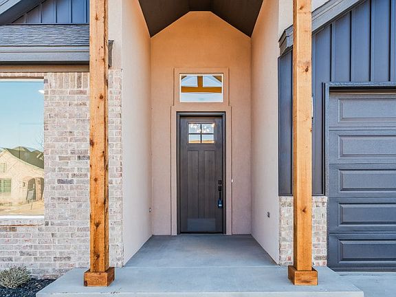A modern house entrance with a dark front door, tall wooden pillars, brick and siding exterior, and