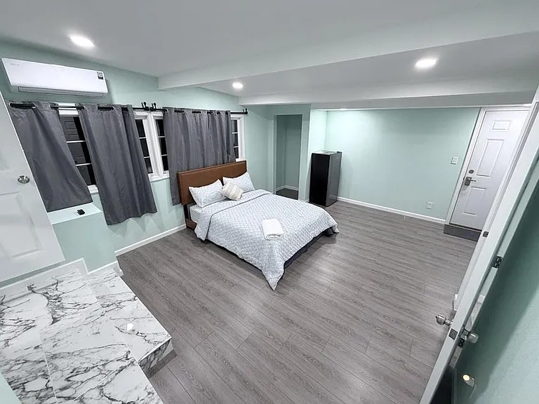 Spacious bedroom with updated flooring, recessed lighting, and multiple windows with curtains, plus in-room mini fridge.