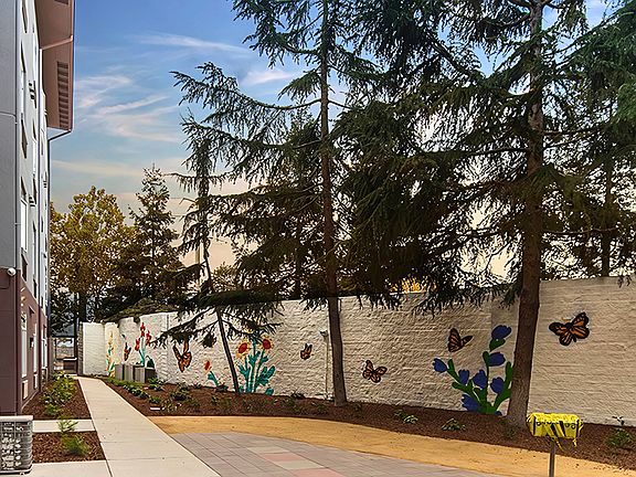 Peaceful outdoor walkway accented by vibrant murals and lush trees, perfect for a refreshing stroll