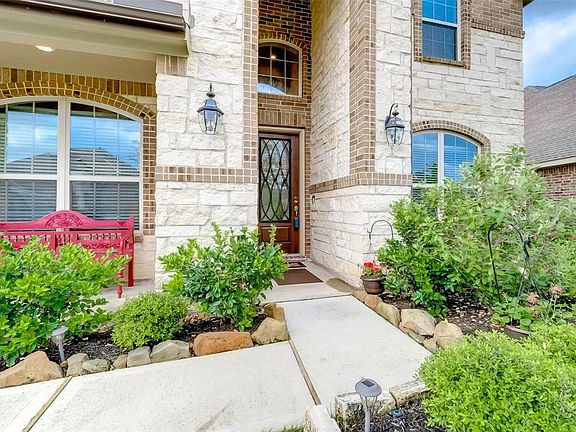 A close-up of the extended porch featuring stylish rich wood front door with ornate wrought iron pane. Notice the charming seating area to the left hand side.