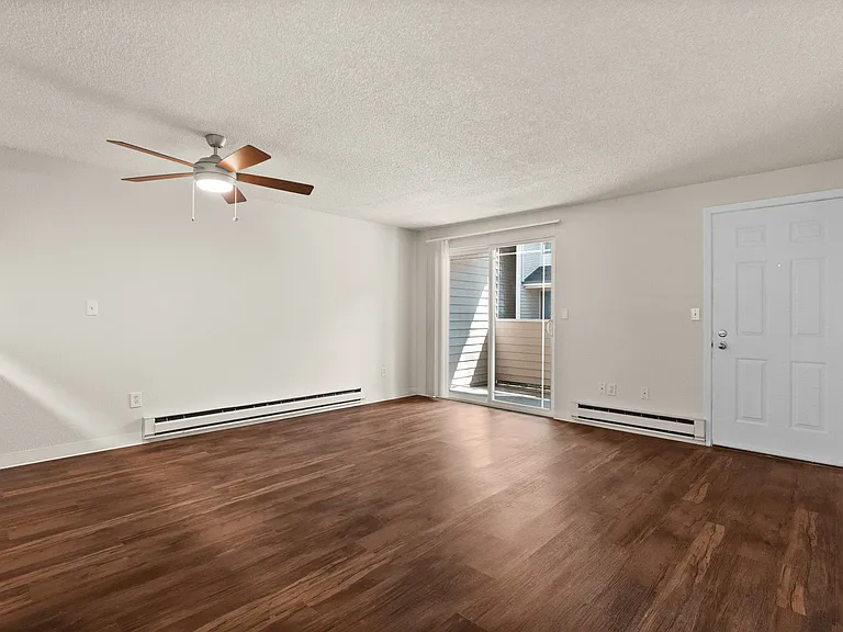Spacious living room with elegant wood flooring and ceiling fan, enhanced by natural light through sliding glass doors. Spacious living room with elegant wood flooring and ceiling fan, enhanced by natural light through sliding glass doors.