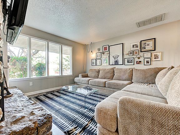 Living room with oversized couch, many windows and mounted smart TV. The windows now have light coverings for privacy.