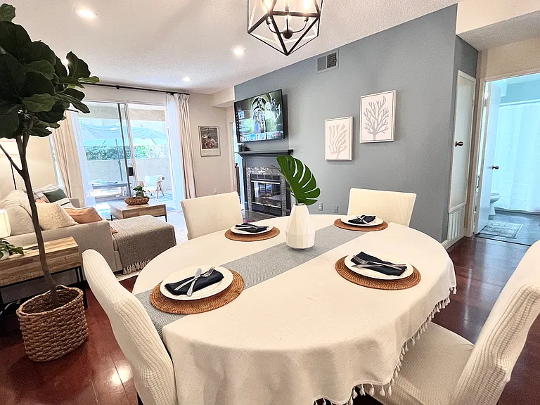 Elegant dining table for 4-6 guests with slipcovered chairs, overlooking the 65" Smart TV.