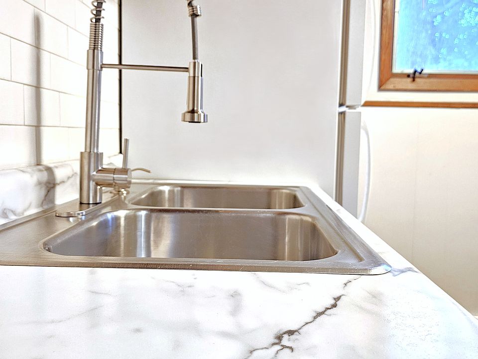 New faucet fixture and soap dispenser, subway tile backsplash, and faux marble countertop.