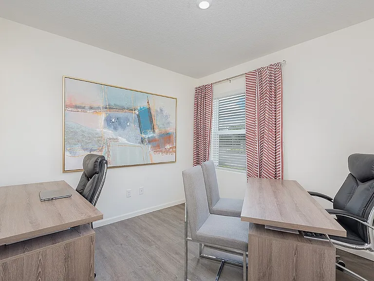 Bright and inviting home office with modern desks and sleek chairs, highlighted by a large abstract painting and natural light from a window with chic curtains.