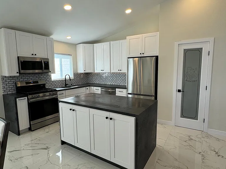 Kitchen with new SS appliances, quartz countertops, white shaker cabinets, workstation sink, island and under cabinet lighting.