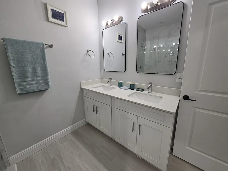 Updated bathroom with a double-sink vanity, ample cabinet storage, and a glass-enclosed shower with tile surround.