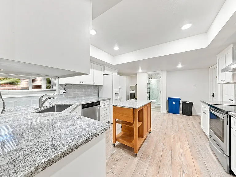 Updated kitchen with granite counters, stainless appliances, ample cabinetry, and a movable island for added prep space.