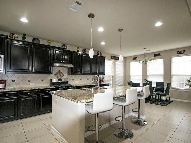 Kitchen featuring appliances with stainless steel finishes, pendant lighting, backsplash, a kitchen island with sink, and light stone countertops.
