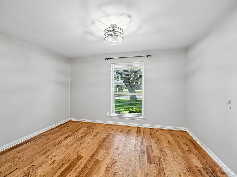 Light-filled room featuring wood-finish flooring, a single window with horizontal blinds, and an overhead decorative light fixture