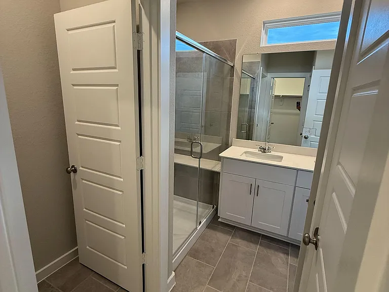 Bathroom with tiled flooring, a single-sink vanity with storage, and a glass-enclosed tub/shower with tile surround.