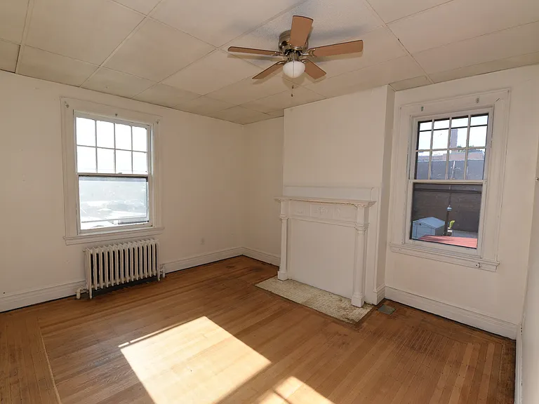 Spacious bedroom with original hardwood floors, abundant natural light, a ceiling fan, classic architectural details, and built-in storage.