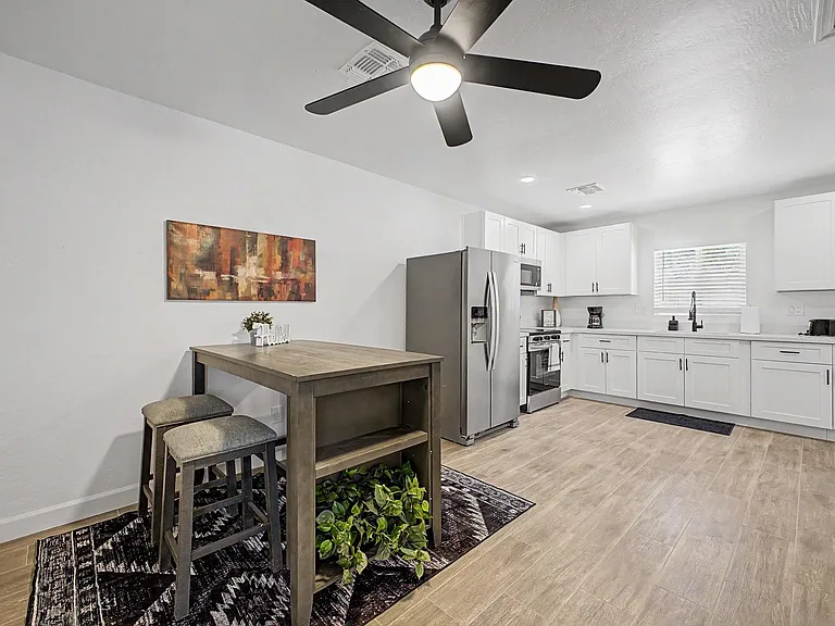 Kitchen with white cabinetry, stainless appliances, ample counter space, and a small dining nook under a ceiling fan.