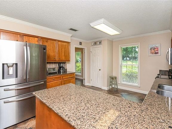 Spacious kitchen featuring an island with granite countertops, wood cabinetry, stainless steel refrigerator, and tiled flooring