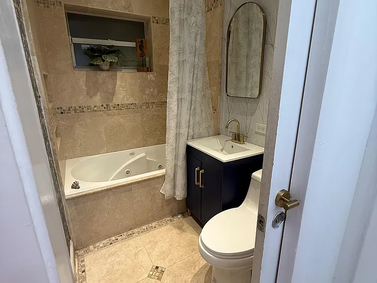 Tiled bathroom with a tub/shower combo, updated vanity, and a wall mirror, plus a small window for ventilation.