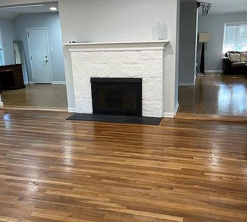 Unfurnished living room featuring dark wood-style floors, a stone fireplace, crown molding, and recessed lighting