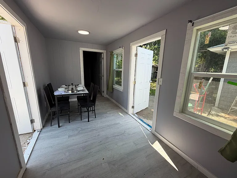 Dining area with a table set for four, durable flooring, and large windows plus direct access to the yard.