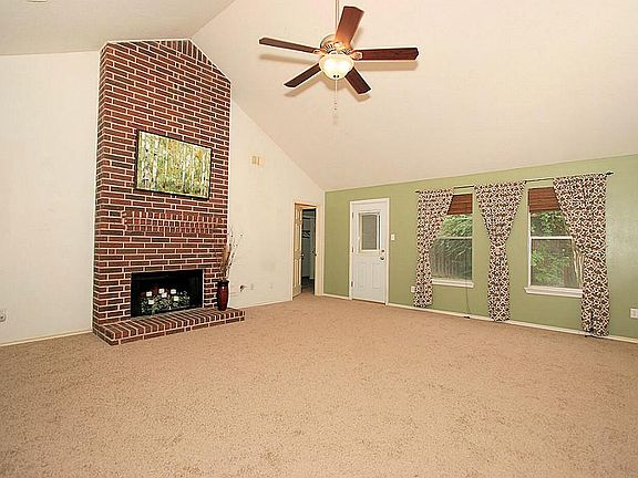 A view of the oversized family room that features new carpet, vaulted ceiling, gorgeous brick fireplace, ceiling fan and plenty of natural light!