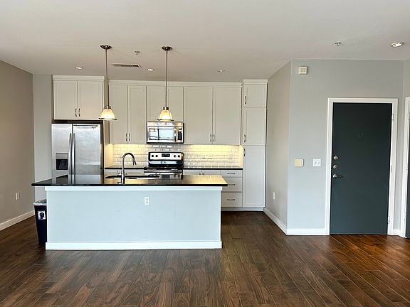 Kitchen with appliances with stainless steel finishes, decorative backsplash, hanging light fixtures, white cabinetry, and an island with sink