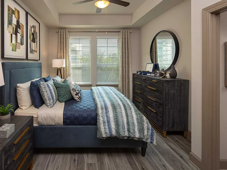 Bedroom with queen sized bed, dresser and nightstand, wood like floor, ceiling fan and large windows
