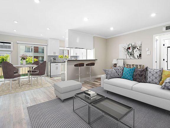Hardwood floored living room with view of dining room, bar seating in kitchen, and balcony.