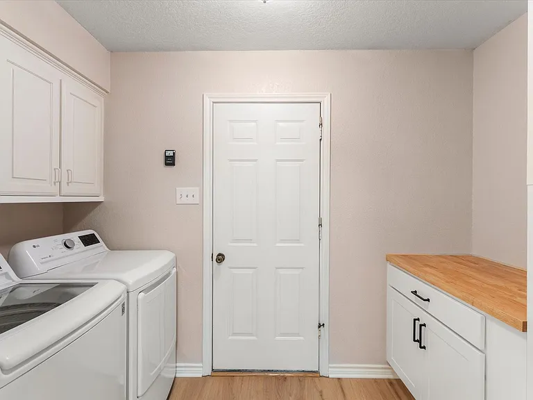 Laundry area featuring wood-finish flooring, white cabinetry, a built-in wood countertop, and a solid panel door
