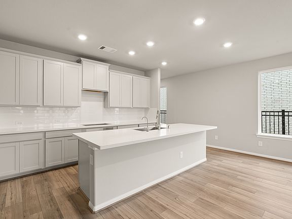 The light and bright kitchen features white cabinetry, quartz countertops and a modern backsplash ti