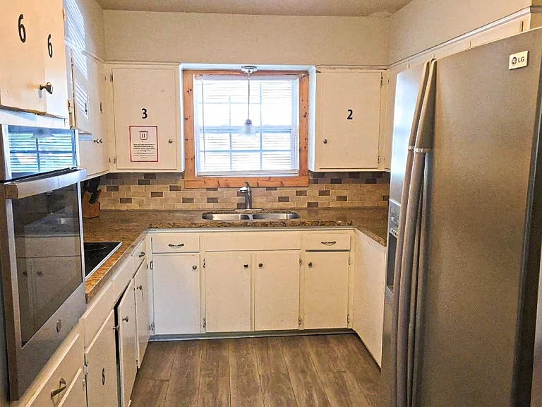 Galley kitchen with ample cabinet storage, electric range and wall oven, double-basin sink, and a window over the counter.