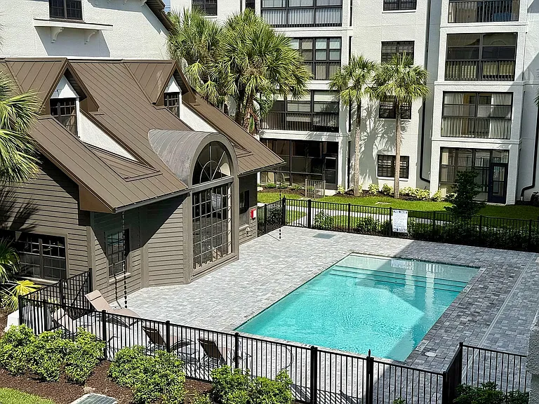 Luxurious apartment building showcasing a sparkling outdoor pool surrounded by lush greenery and elegant architecture.