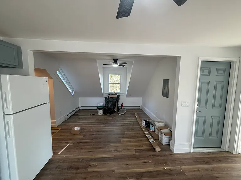 Great room facing east. Beyond the refrigerator to the left is the foyer. Door is to the front stairway. To the right is the bedroom.