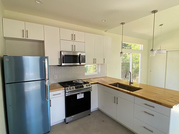 Kitchen with brand new appliances. Refrigerator is stainless steel, wrapped here in blue for protection. Kitchen counter two pendant lights and has room for 3 barstools.