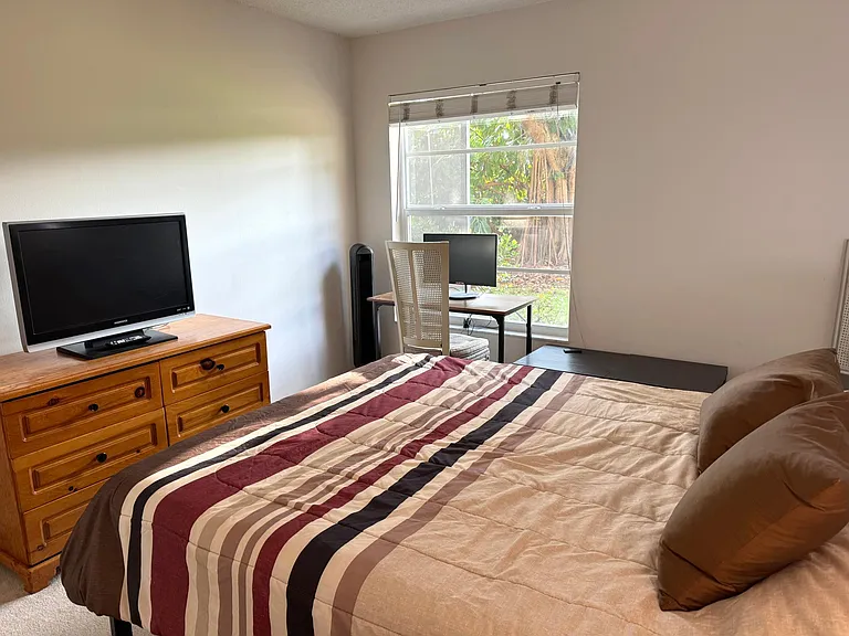 Second bedroom looking at desk facing window overlooking large tropical yard