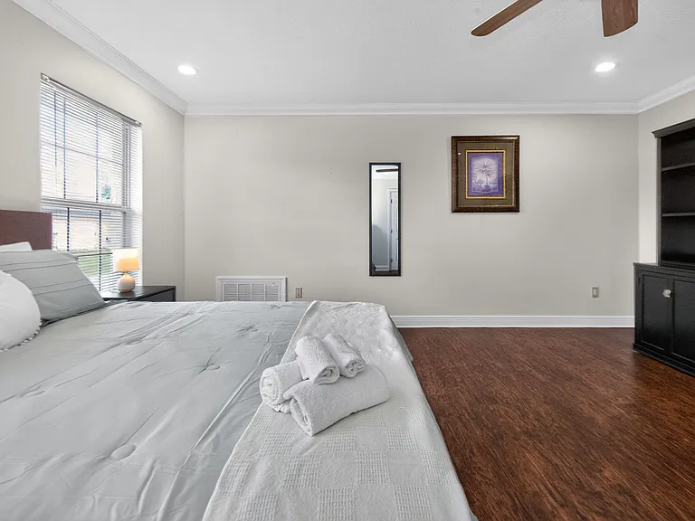 Spacious bedroom with hardwood floors, ceiling fan, large window with blinds, and a built-in storage cabinet.