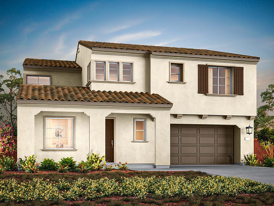 A two-story Mediterranean-style house with a tiled roof, surrounded by lush greenery and a well-mani