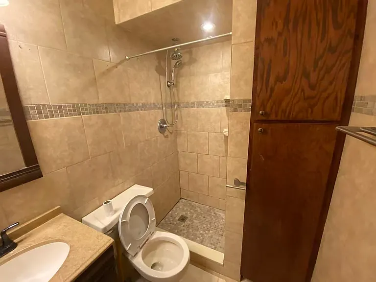 Bathroom on the first floor featuring a spacious walk-in tiled shower, modern fixtures, built-in storage, and a vanity with countertop space. Neutral finishes create a clean and contemporary look.