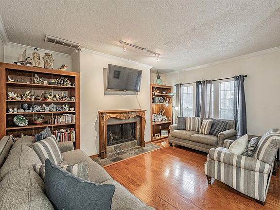Living room featuring crown molding, a textured ceiling, track lighting, a tiled fireplace, and hardwood / wood-style floors and built in shelves.