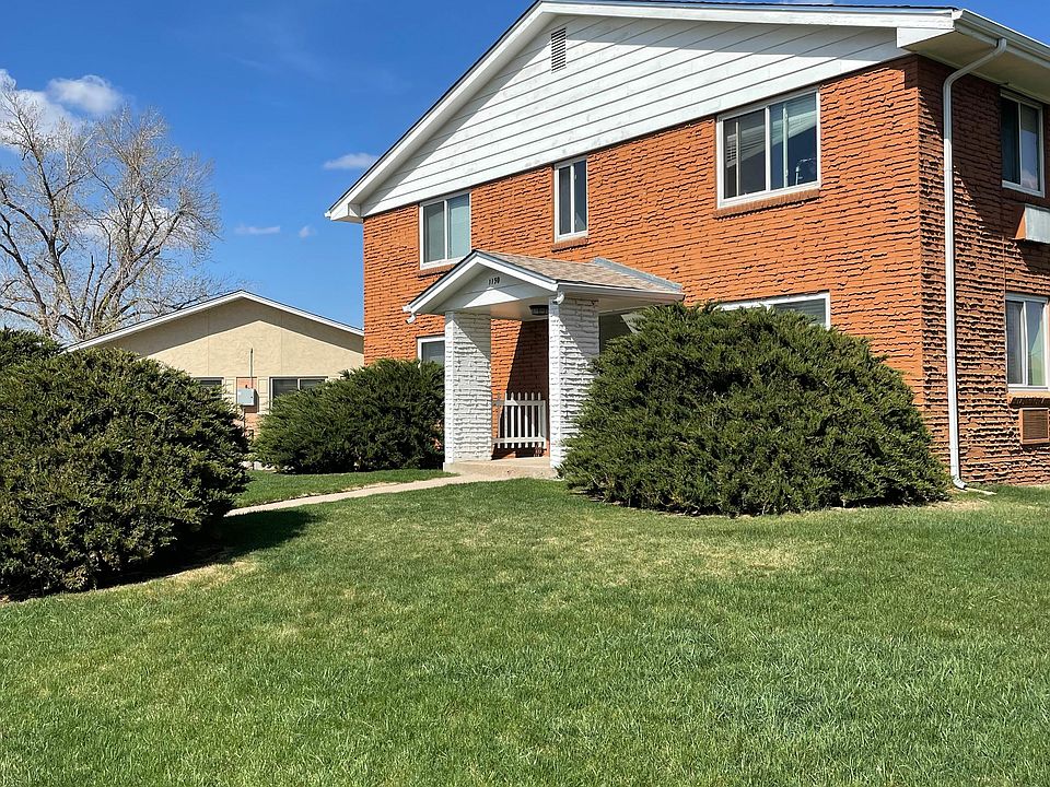 Inviting brick apartment building with manicured lawn and bright windows under a clear blue sky.